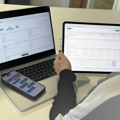 Person working on a laptop and tablet displaying product costings and purchase order management software.