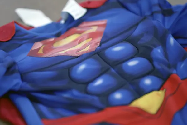 Close-up of a padded children's superhero costume with a printed red and yellow emblem on a blue muscle suit.