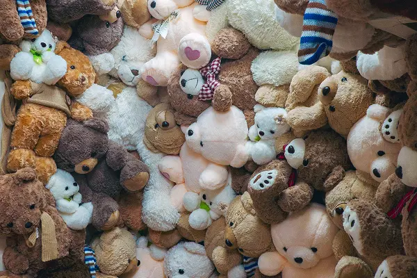 Assorted plush teddy bears in various colours piled together.