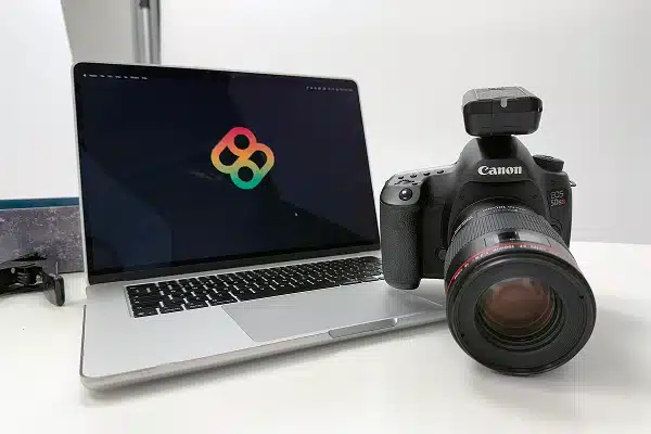 Canon DSLR camera placed beside a laptop displaying the Bombiix logo on a photography studio table.