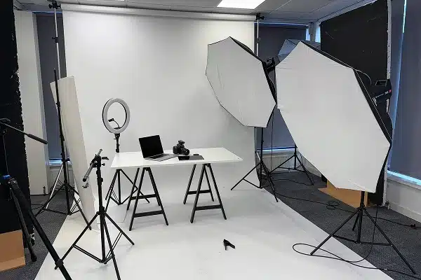 Photography studio setup with lighting equipment, camera, and laptop on a white backdrop.