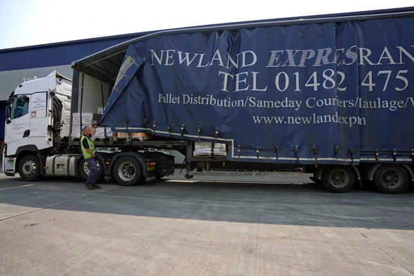 Logistics worker unloading a Newland Express freight truck outside a warehouse.