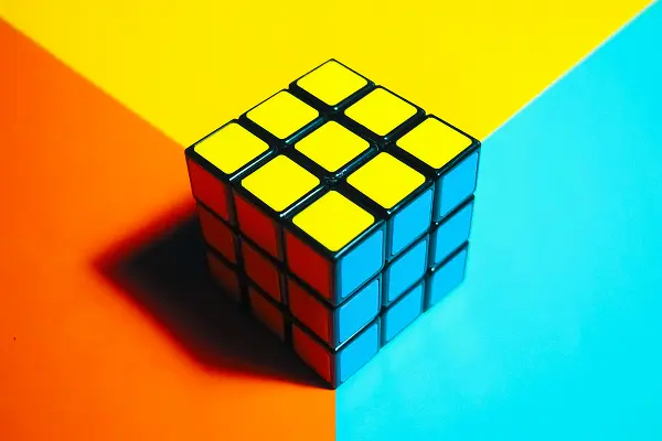 Rubik’s cube with yellow, blue, and orange faces placed on a multicolour background split into yellow, orange, and blue sections.