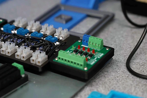 Close-up of an electronics circuit board with wiring and connectors on a workbench.