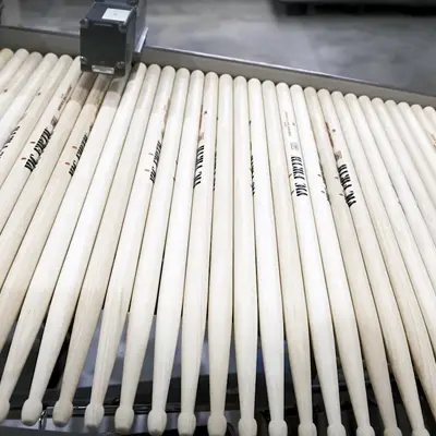 Row of wooden drumsticks being processed on an automated production line.
