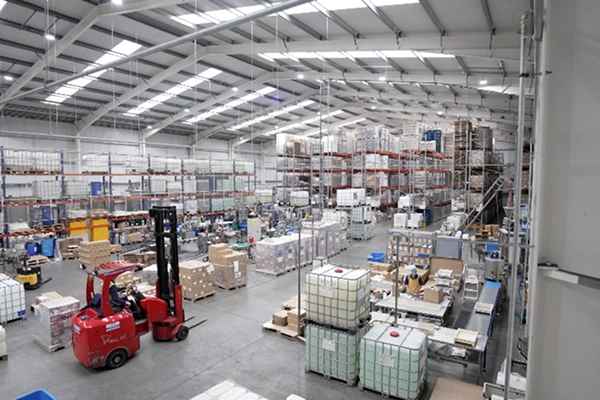 Large warehouse interior with stacked shelves, pallets, and forklifts in operation.
