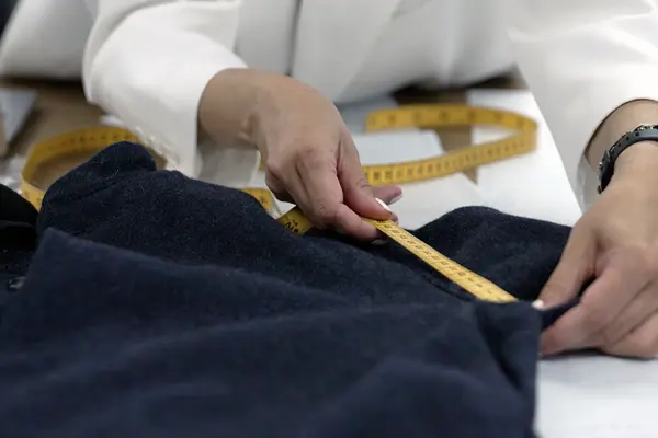 Close-up of a person measuring a garment sample with a yellow tape measure on a design table.