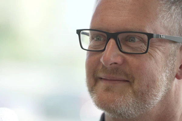 Close-up of a smiling man wearing black-framed glasses looking confidently to the side.