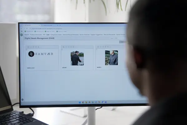 Person viewing a Digital Asset Management (DAM) interface on a computer screen displaying brand logos and product images.