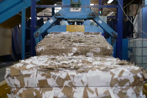 Stacked and compacted cardboard waste inside a recycling facility with industrial machinery.
