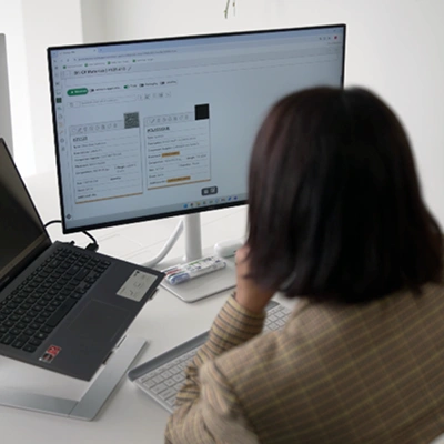 Person reviewing product data sheets on a large monitor connected to a laptop in an office setting.