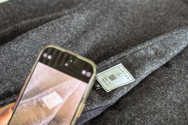Person scanning a garment care label on grey fabric with a smartphone.