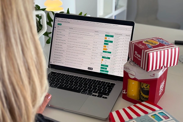 Person reviewing custom product reporting data on a laptop with packaging samples on the desk.