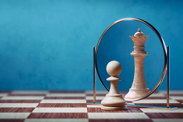Chess pawn looking into a mirror and seeing its reflection as a queen on a chessboard.