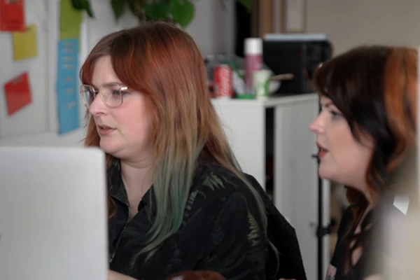 Two women working together at a computer in a modern office environment.
