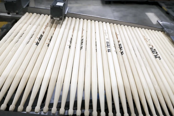 Row of wooden drumsticks being processed on an automated production line.