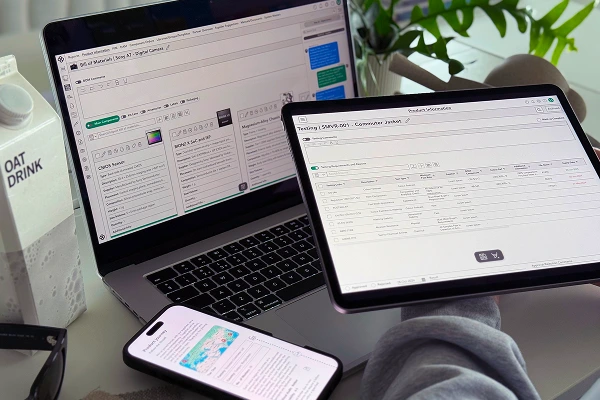 Person using multiple devices to manage product information, testing records, and traceability through a PLM interface.