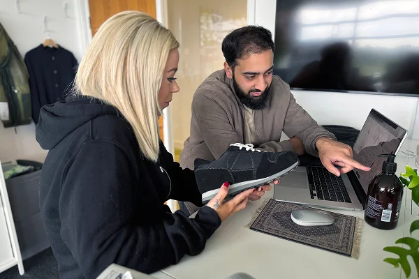 Two team members collaborating on a shoe design, referencing digital specifications on a laptop.