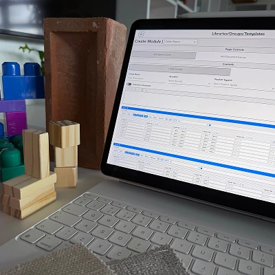 Tablet displaying a configuration and module creation interface, surrounded by fabric swatches, wooden blocks, and a brick.