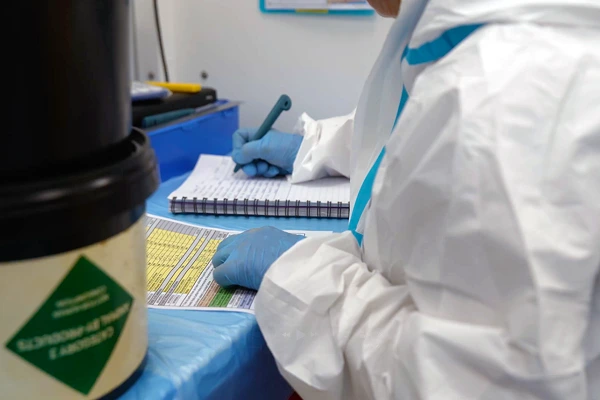 Quality control technician in PPE recording data in a laboratory environment.