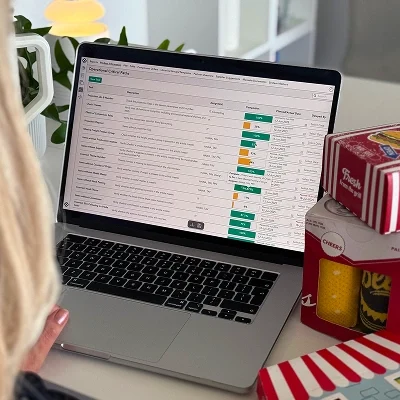 Person reviewing custom product reporting data on a laptop with packaging samples on the desk.