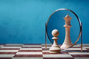 Chess pawn looking into a mirror and seeing its reflection as a queen on a chessboard.